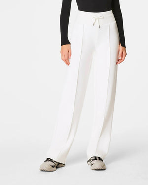 A person wearing a black long-sleeve top and high-waisted SPANX AirEssentials Luxe Straight Leg Pants in white stands with their back to the camera, highlighting the pant's design and fit, made from super-soft spacer fabric.