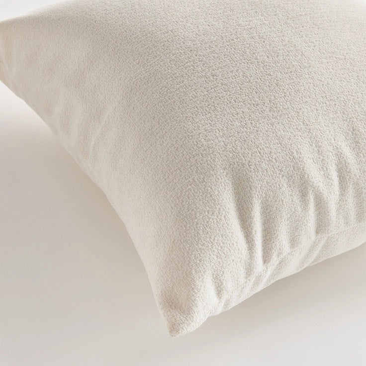 A close-up side view of the COOPER SQUARE INDOOR-OUTDOOR PILLOW 20" by NAPA HOME AND GARDEN against a plain, light background. The image showcases the pillow's white, textured Jacquard fabric and stitching detail, with the zipper partially visible on the edge.