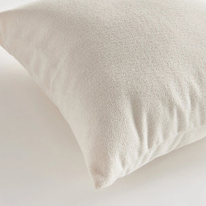 A close-up side view of the COOPER SQUARE INDOOR-OUTDOOR PILLOW 20" by NAPA HOME AND GARDEN against a plain, light background. The image showcases the pillow's white, textured Jacquard fabric and stitching detail, with the zipper partially visible on the edge.