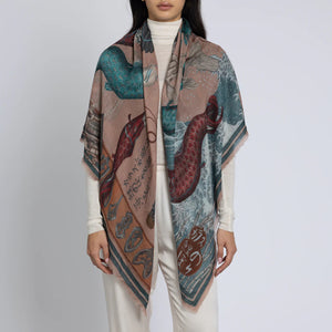 A person adorned in a long, striking SABINA SAVAGE - KOINOBORI KARASU CASHMERE SHAWL 135CM by SABINA SAVAGE ENGLAND, showcasing intricate fish and wave designs over a white outfit. The shawl is embellished with stylized script and features shades of blue, red, and beige.