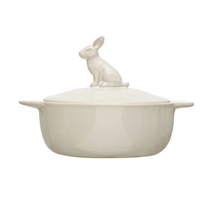 The STONEWARE BAKER WITH RABBIT FINIAL by CREATIVE COOP is a cream-colored stoneware casserole dish with side handles and a lid topped with a sitting rabbit figure as the handle.