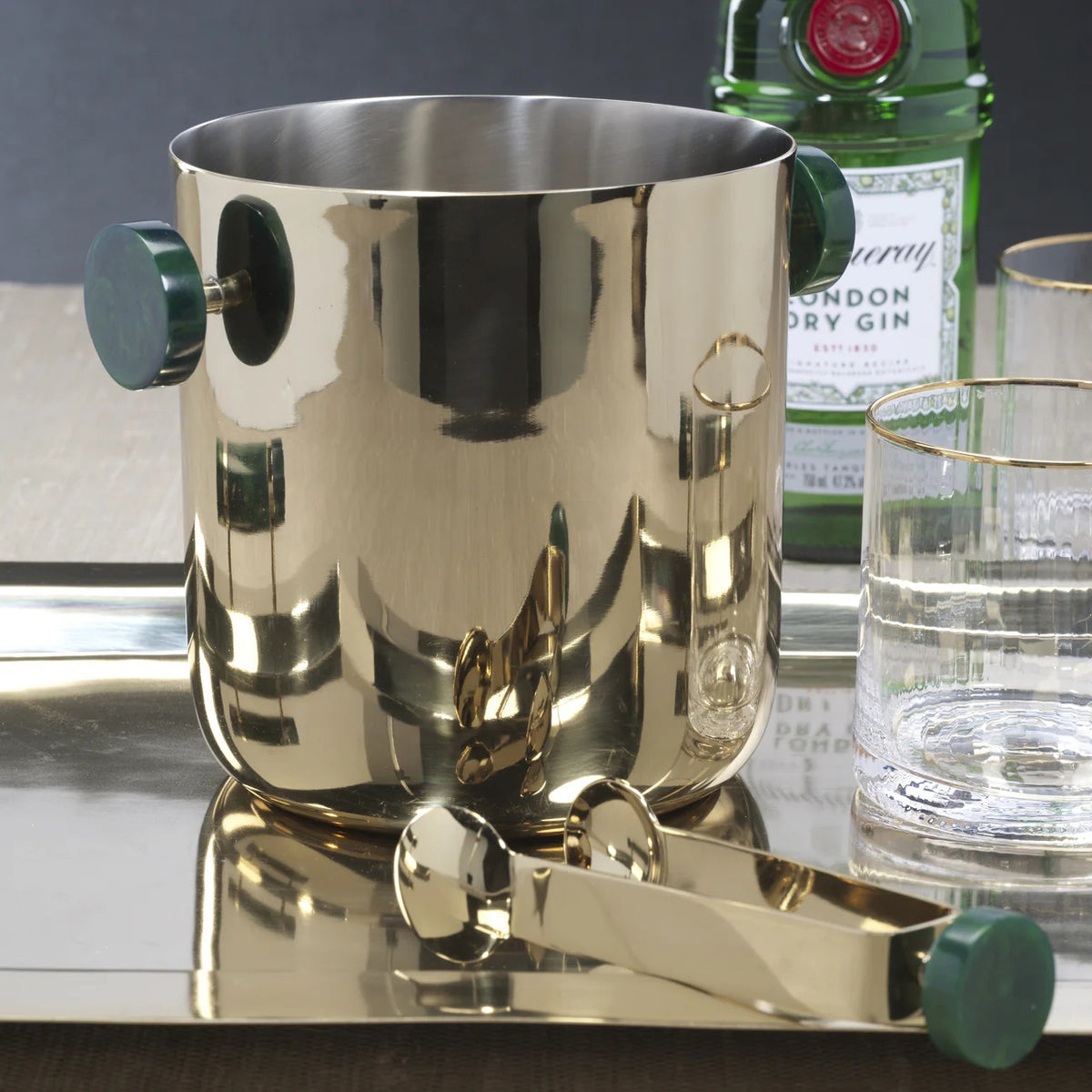 The SPIGA ICE BUCKET - GREEN ACCENTS by ZODAX features a shiny metallic, cylindrical design with two dark green handles, crafted from alloy resin for stylish home decor and shown against a white background.