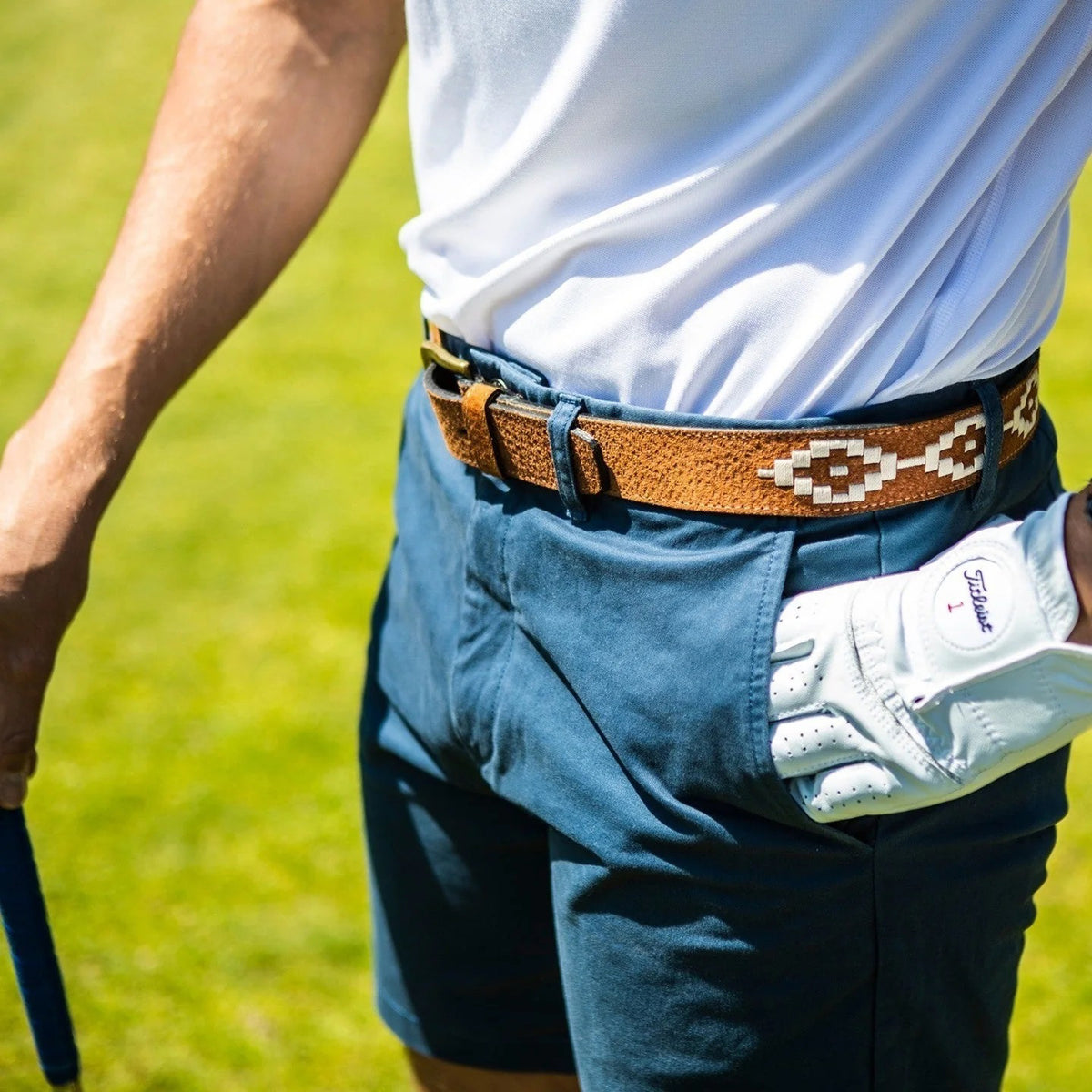 The LA MATERA - EL CAMPO POLO BELT by LA MATERA features brown saddle leather, a gold buckle, textured surface, and white hand-embroidered geometric patterns, coiled neatly against a white background.