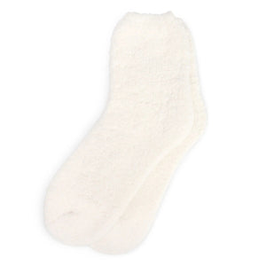 A person stands on a white background, wearing a cozy, textured white robe, KASHWERE - ADULT SOCKS by KASHWERE, and white slippers. Only the lower half of the body is visible. The attire appears ultra-plush and comfortable, ideal for lounging or relaxation.