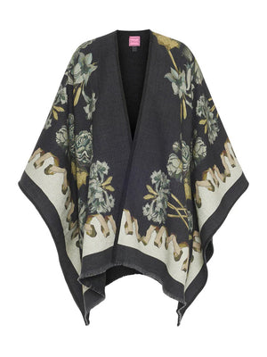 The "FRANCO FERRARI - ROSES AND DAFFODILS WOOL PONCHO" from the FRANCO FERRARI brand is a dark shawl adorned with a beige and green floral pattern featuring roses and daffodils. It has a fringed hemline and an asymmetrical shape for a draped, relaxed fit, giving it an elegant and nature-inspired appearance. This wool poncho is made in Italy.