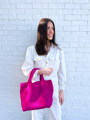 A person wearing a white shirt and dark pants holds the PARKER AND HYDE - WOVEN TOTE BAG with two handles. Their arm, adorned with a gold bracelet, stands out against a plain, light-colored background.