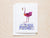 Introducing the FLAMINGO CARD by PETAL PEOPLE PRESS: A charming and unique greeting card showcasing a whimsical flamingo illustration made from pressed pink and purple flower petals, elegantly standing among light blue blossoms on a beige background.