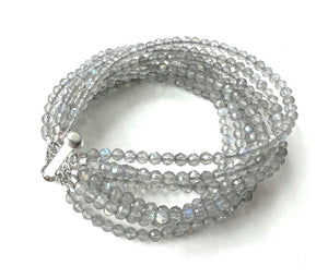 The ANN LIGHTFOOT - NINE STRAND FACETED LABRADORITE CUFF features translucent, faceted grey beads that reflect light for a subtle iridescent effect, coiled neatly and secured with a silver clasp.