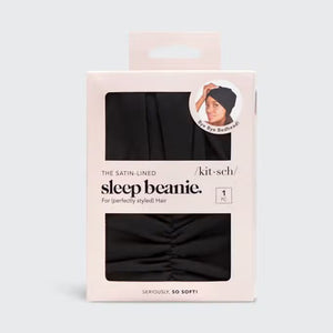 Packaging for the SLEEP BEANIE WITH SATIN LINING by KITSCH. The primarily white box features a cut-out displaying the black beanie inside. It advertises "Bye Bye Bedhead" and highlights that it’s "Seriously, SO SOFT!" Designed to prevent hair breakage, a small image shows a person wearing the jersey bonnet.