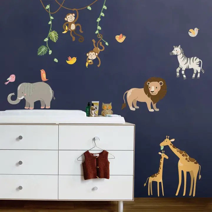 SIMPLE SHAPES - JUNGLE ANIMALS REMOVABLE WALL DECALS by SIMPLE SHAPES offer a vibrant collection of cartoon animals, including monkeys swinging from vines, colorful birds, a playful zebra, a giraffe and its calf, an adorable lion, and an elephant with a bird perched on its back. To enhance the scene, two wooden crates filled with stuffed toys and books are placed below for added charm.