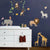 SIMPLE SHAPES - JUNGLE ANIMALS REMOVABLE WALL DECALS by SIMPLE SHAPES offer a vibrant collection of cartoon animals, including monkeys swinging from vines, colorful birds, a playful zebra, a giraffe and its calf, an adorable lion, and an elephant with a bird perched on its back. To enhance the scene, two wooden crates filled with stuffed toys and books are placed below for added charm.