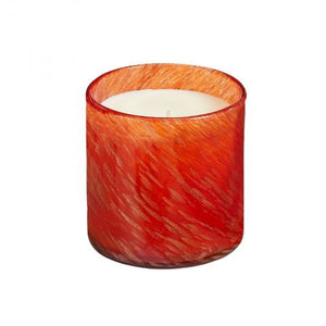 A glowing, orange-colored candle made from soy wax is placed next to a red box labeled "LAFCO - ABSINTHE PLUM HOLIDAY CANDLE 15.5OZ." The scent of black plum and sandalwood permeates the air. The candle's warm, inviting glow is beautifully enhanced by the rich red background.