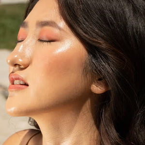 A close-up of a person with curly dark hair, a serious expression, and warm makeup featuring the universally flattering, weightless JASON WU - HOT FLUFF LIP/EYE/CHEEK by JASON WU BEAUTY on their face. They are looking directly at the camera with a neutral background.