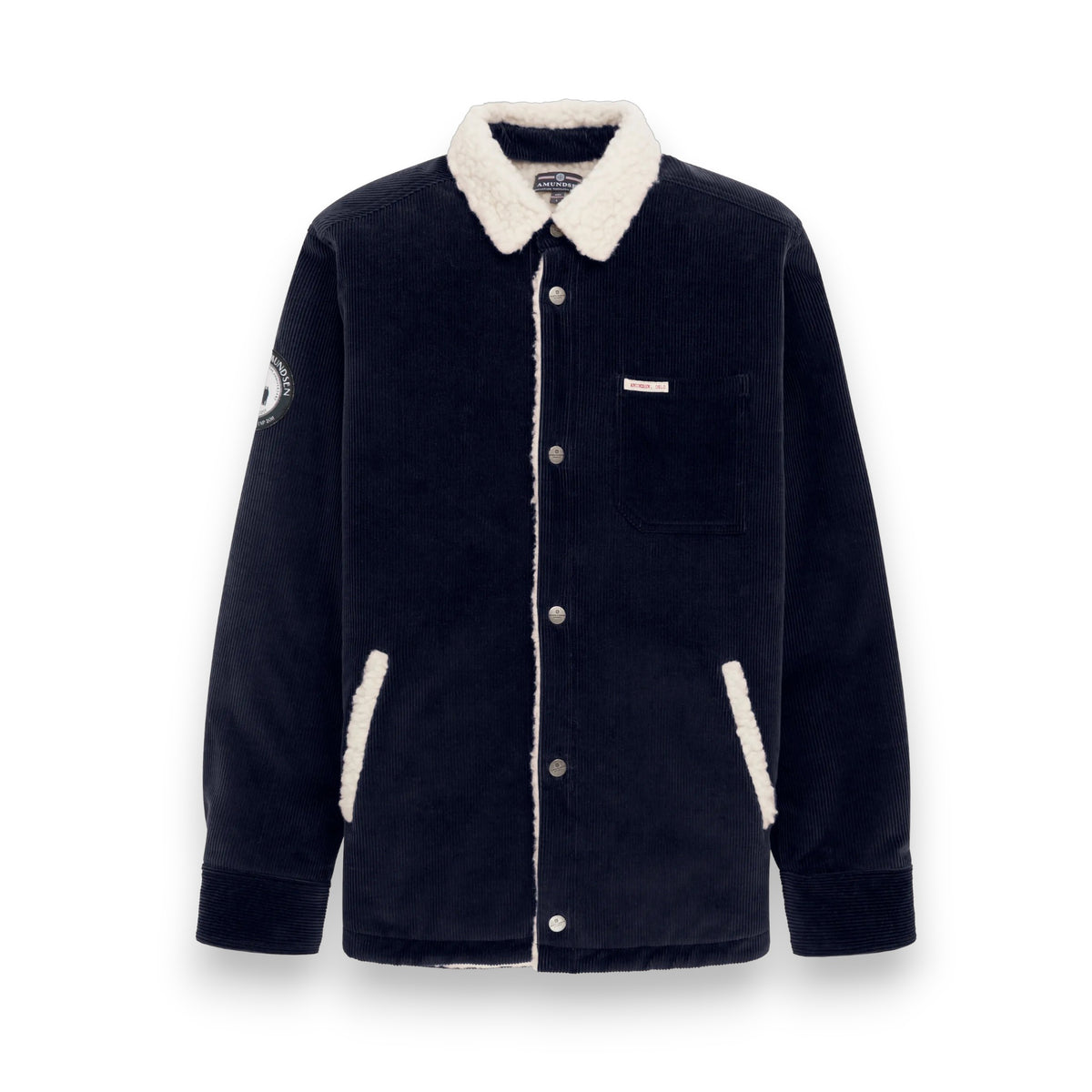 The AMUNDSEN SPORTS Harvester Overshirt in True Navy is a stretch cotton corduroy jacket with white sherpa trim, chest and side pockets, snap buttons, and a circular left-sleeve patch.
