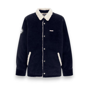 The AMUNDSEN SPORTS Harvester Overshirt in True Navy is a stretch cotton corduroy jacket with white sherpa trim, chest and side pockets, snap buttons, and a circular left-sleeve patch.