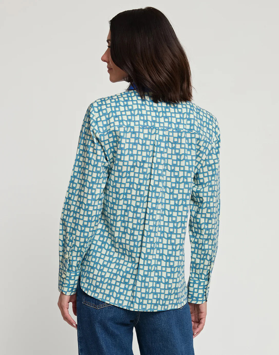 A person with shoulder-length dark hair is standing with their back to the camera, wearing a relaxed-fit HINSON WU - MARGOT LONG SLEEVE MAZE GEO PRINT SHIRT and blue jeans. The background is plain white.