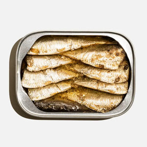 An aerial shot captures an opened tin of FISHWIFE - LITTLE SARDINES, glistening in Spanish olive oil against a pristine white backdrop. The sardines are meticulously arranged in overlapping layers, displaying their silvery scales and underscoring their status as a nutritional superfish.