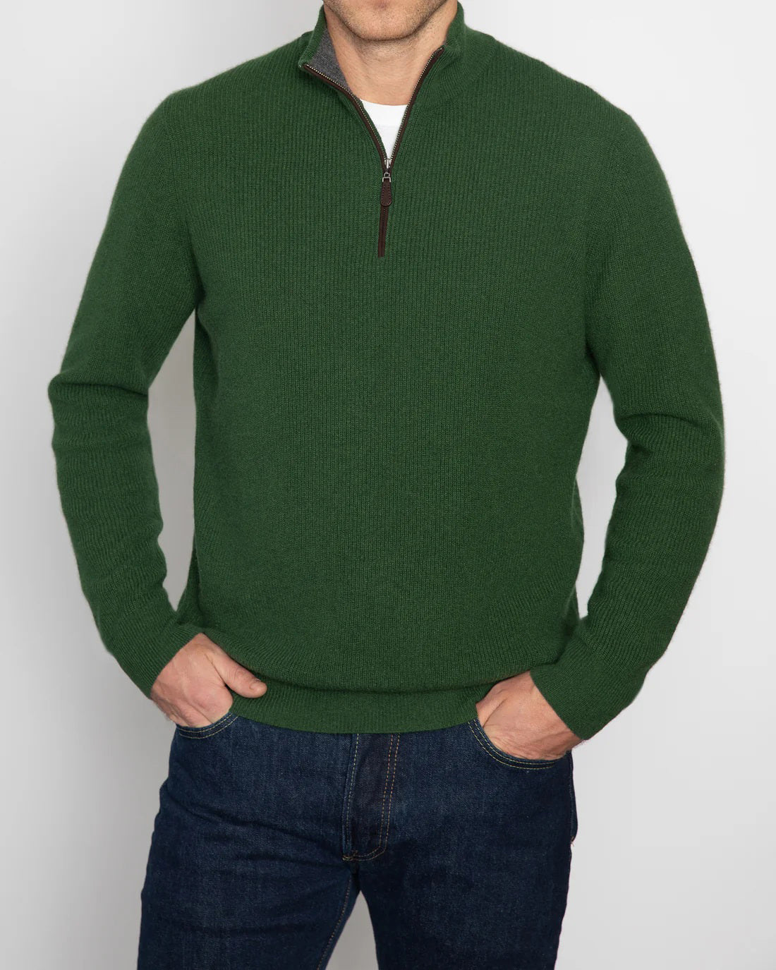 A person wearing a maroon KINROSS CASHMERE - MENS CASHMERE SUEDE TRIM RIB QUARTER ZIP MOCK sweater stands with hands in pockets, paired with dark blue jeans against a plain white background.