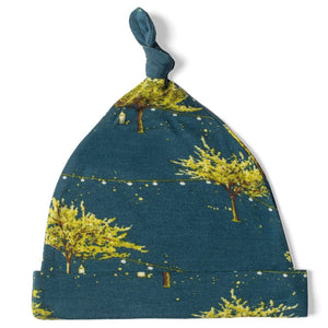 A Bamboo Knotted Hat from MILKBARN, in blue, featuring a top knot and decorated with a pattern of yellow-green trees and firefly prints. The MILKBARN - BAMBOO KNOTTED HAT FIREFLY is designed for sensitive skin and includes a folded brim with a pointed top.