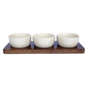 Three small stoneware bowls are placed on a rectangular mango wood tray. The bowls are evenly spaced and aligned in a row. The MANGO WOOD TRAY WITH BOWLS by CREATIVE COOP features a minimalist design with a natural and rustic aesthetic.