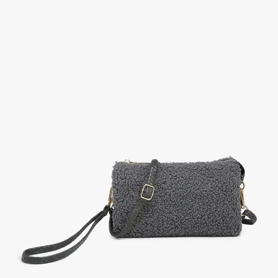 The SHERPA WRISTLET CROSSBODY from JEN & CO features plush, curly wool-like material in gray, complemented by gold hardware and a slim, adjustable shoulder strap. Its elegant simplicity is highlighted against the plain white background.