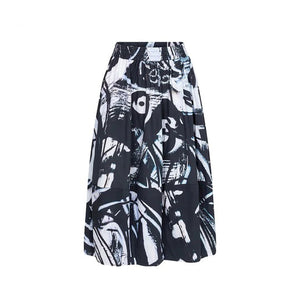 The JUJU CIRCLE SKIRT by TALKING WALLS is an A-line midi-skirt adorned with a striking black and white abstract pattern. It showcases high-end tailoring, featuring a high waist, an elastic waistband, and a pleated design that provides a flowing and voluminous appearance. The bold print includes diverse brush strokes and shapes.