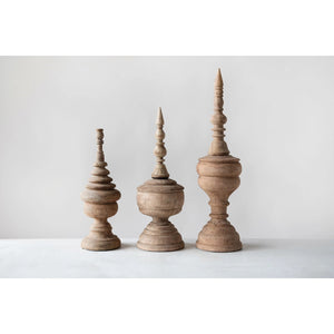 Displayed against a white background are three intricately carved CARVED MANGO WOOD FINIALS (LARGE) by CREATIVE COOP, each featuring unique ornamental designs with a rounded base and a pointed, spire-like top. Perfect as table accents or fireplace mantel decor, the natural finish highlights the wood's grain and texture.