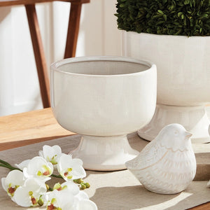 The ALBIE FOOTED CACHEPOT by NAPA HOME AND GARDEN is a white, ceramic pedestal bowl featuring a smooth, shiny white glaze with a slightly rounded top edge. Elevated on a short, cylindrical base, its traditional shape and minimalist design make it an ideal centerpiece. Subtle crackle patterns on the surface add texture and charm.