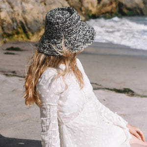 The WYETH HATS - THE LOLO is a hand-crocheted textured woven bucket hat by WYETH, featuring black, white, and beige on a plain white backdrop. The customizable fit ensures comfort while showcasing style.