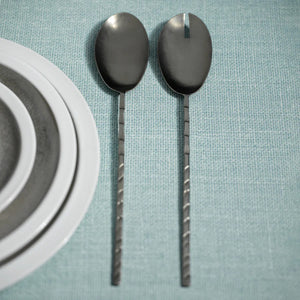 Displayed are two elegant, long-handled servers from the ZODAX TWISTED HAMMERED PEWTER collection. One is a traditional serving spoon, and the other is a slotted serving spoon with a notch at the top. Both feature a textured, twisted design on the handles. Dimensions vary slightly with each size for versatile use in your kitchen.