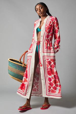 A barefoot person stands against a gray backdrop wearing the HOPE FOR FLOWERS - BAND COLLAR SHIRTDRESS, which features a cream background with vertical stripes, long red florals, a cinched waist, and long sleeves.