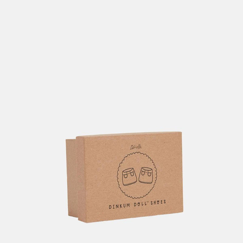 A close-up of a baby wearing OLLI ELLA USA DINKUM DOLL SHOES in Mallow Pink and white socks. The baby is seated on a soft, pale pink textured blanket, dressed in light brown clothing. Only the lower half of the baby&#39;s body is visible.