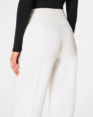 A person wears a black long-sleeve top and SPANX AireEssentials Luxe Straight Leg Pant with a drawstring waist. Relaxed, they pair them with gray shoes featuring black straps. Against a white background, the outfit from SPANX exudes effortless comfort.