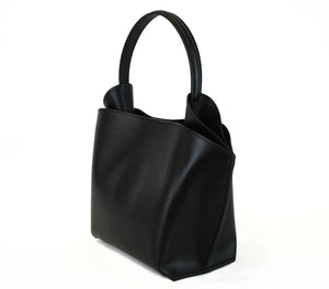 Introducing the RIGID LEATHER HANDBAG by LEATHER COUNTRY, a stylish black handbag with a unique geometric shape, featuring a top handle and a removable shoulder strap. The bag boasts gold-tone hardware, a magnetic closure, and an unlined interior spacious enough for your daily essentials.