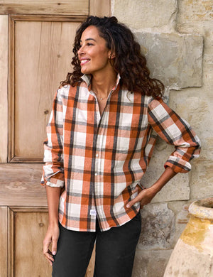 The FRANK & EILEEN Eileen Relaxed Button Up Shirt in Italian Flannel Pumpkin Plaid is a long-sleeved, button-up design featuring a flattering button placement at the bust and a classic collar. It showcases an orange, white, and brown plaid pattern with stylishly rolled-up sleeves. Additionally, the brand label is visible on the inside of the collar.