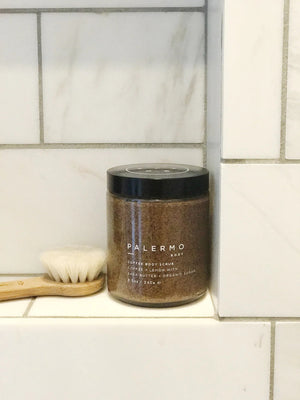 A jar of PALERMO BODY - COFFEE & LEMON BODY SCRUB is shown against a white background. The organic coffee scrub, featuring lemon, shea butter, moisturizing coconut oil, and organic sugar, comes with a black lid. The label details the product information and the quantity is 8.5 oz / 240 g.