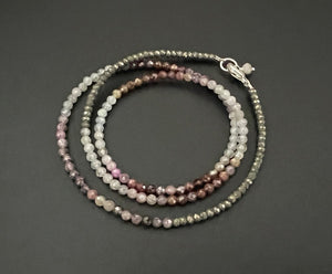 The ANN LIGHTFOOT - TRIPLE WRAP VARIEGATED SPINEL BRACELET features small, faceted spinel beads in a range of colors, including shades of gray, pink, brown, and beige. Coiled neatly on a dark background, the beads add a subtle shine to this elegant piece.