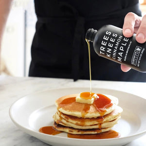 A black bottle with a matching black cap labeled "BUSHWICK KITCHEN - 'TREES KNEES' CINNAMON MAPLE SYRUP" in white text. This 11.5 oz (326g) delight from Bushwick Kitchen combines the rich flavors of cassia cinnamon and pure maple syrup. The label proudly announces that this product was born in Brooklyn, NY.