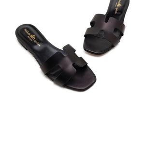 The image depicts the MICHELE LOPRIORE - H SLIDE, a single brown leather slide sandal with an open-toe design. The upper features two wide straps with geometric cutouts. The thin sole appears to be made of light brown wood-like material. Made in Italy by MICHELE LOPRIORE, the sandal is displayed against a plain white background.