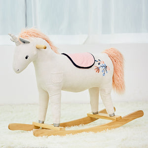 The WONDER AND WISE ASWEETS UNICORN ROCKER features a white fabric unicorn with a unicorn horn, light pink mane and tail, and a light pink saddle. Mounted on a wooden rocker base, it includes magical details such as stitched eyes and a small side pocket for added comfort.