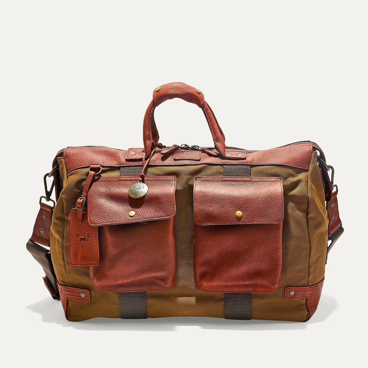 The WILL LEATHER GOODS Canvas and Leather Duffel in Tobacco/Cognac is open to show its roomy interior with a red and black plaid lining. Two matching plaid accessories from WILL LEATHER GOODS are displayed beside the bag.