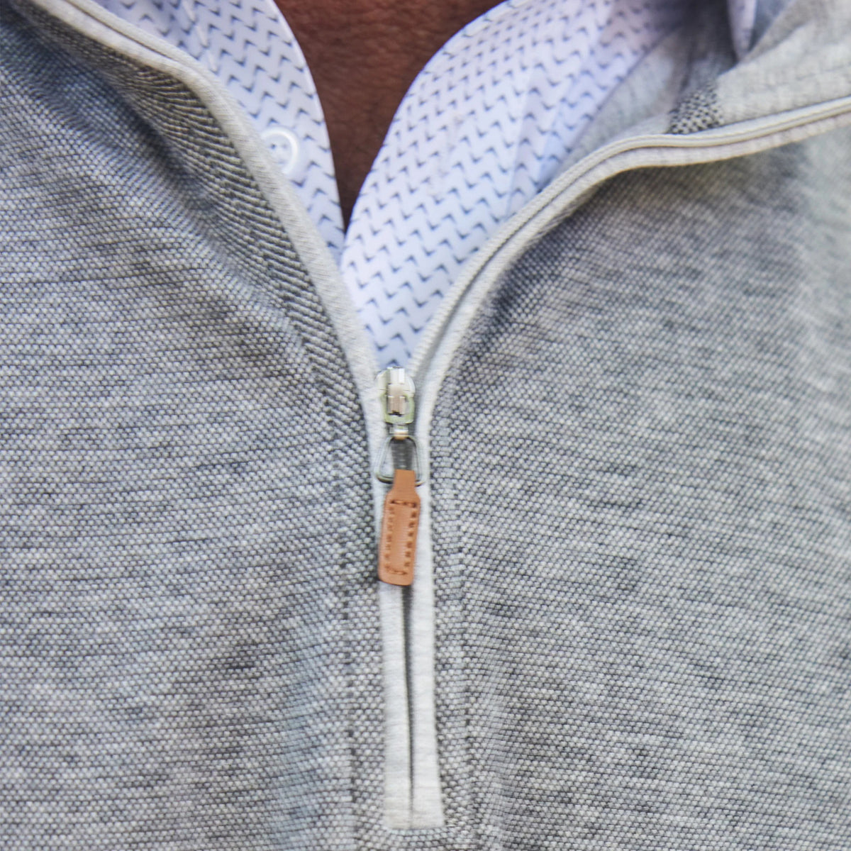 A man with short dark hair and a trimmed beard stands outdoors among green trees, hands in his pockets, wearing the COLLARS AND CO - CLOUD TEXTURED QUARTER ZIP IN GRANITE over a white collared shirt.