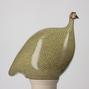 The LES CERAMIQUES DE LUSSAN - LARGE CERAMIC FRENCH GUINEA IN GREY SPOTTED YELLOW is a beautifully handmade ceramic sculpture depicting a guinea hen, with a cylindrical pedestal base. Its body is adorned with grey spots on a yellow background, and the head features a red comb. Crafted in a traditional ceramic workshop by LES CERAMIQUES DE LUSSAN, this piece boasts an elegant glossy finish.