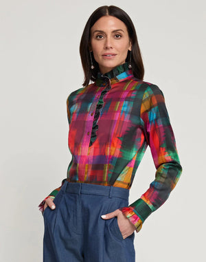 A person with shoulder-length dark hair is seen from behind, wearing the HINSON WU ATHENA LONG SLEEVE SATIN SHIRT in a festive plaid design that includes red, green, blue, and yellow shades. The outfit is complemented by blue pants and the shirt is machine washable for easy care.