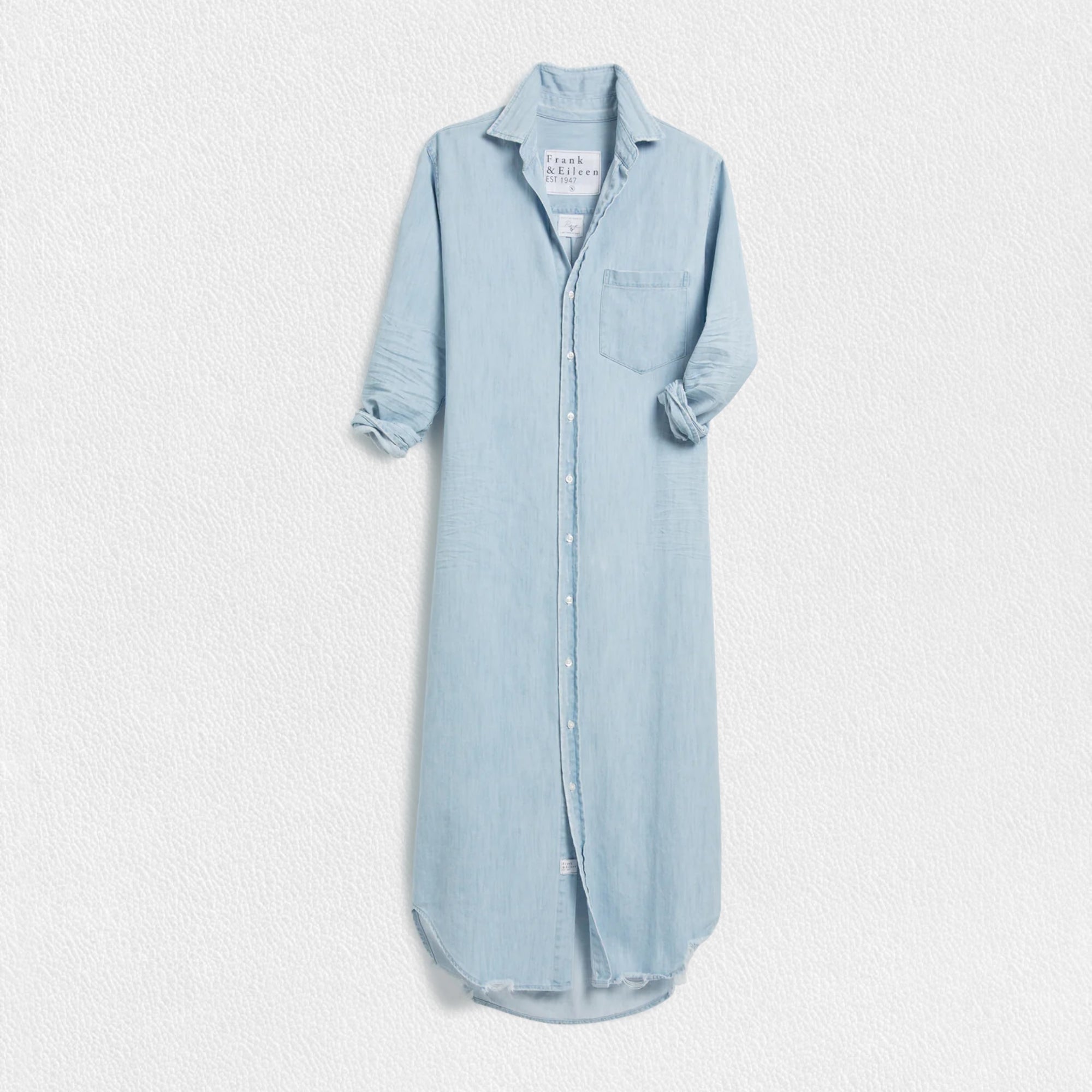 The FRANK & EILEEN Rory Maxi Shirtdress in Famous Denim is a full-length button-up dress featuring a collar, rolled-up sleeves to mid-length, and a single chest pocket. Its sleek, minimalist design embodies that California chic look against a plain white textured background.