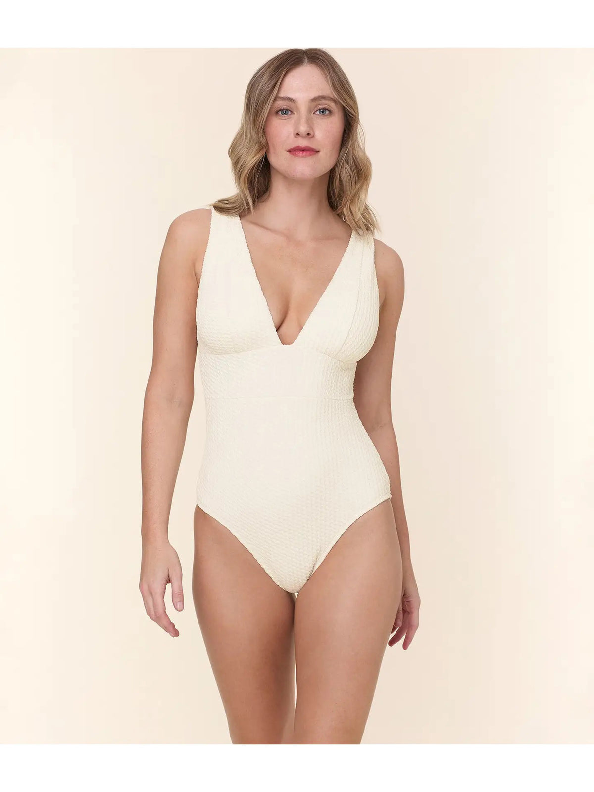 A woman models the ANDIE SWIM The Mykonos One Piece Swimsuit in Textured Wave Gardenia, standing against a plain light beige background.