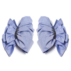 Two large, symmetrical blue fabric cuffs known as CATHERINE OSTI - CINDY CUFFS (m) are positioned side by side on a white background. Each cuff, reminiscent of elegant fabric bracelets, is decorated with a band of dark beads at the center, creating a ruched effect. The cuffs are sophisticated and have a soft, textured appearance.