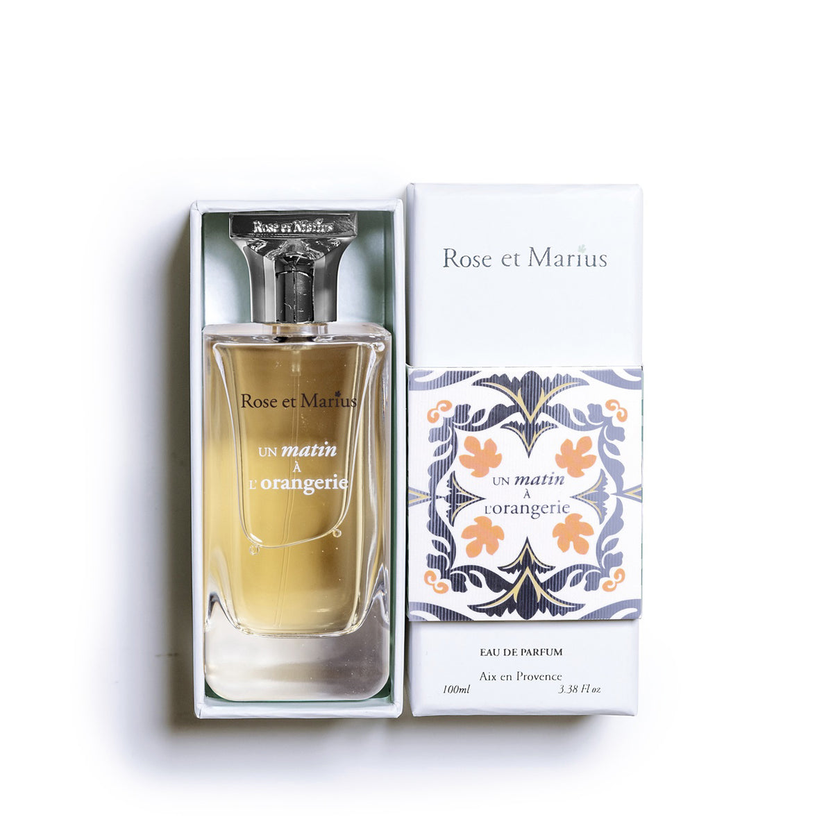 A bottle of ROSE ET MARIUS - A MORNING AT THE ORANGERY EAU DE PARFUM 30ML with a decorative square cap stands beside a circular &quot;Unisexe&quot; label in the top left. The bottle casts a faint shadow on a white background.