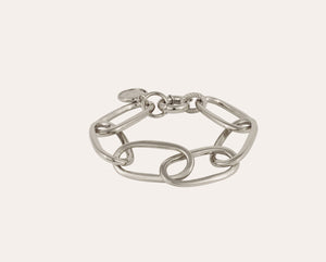 A person with light brown hair and bangs looks down, showcasing the GAS BIJOUX - Maille Oval Bracelet in Silver on their right wrist. Their hands are lightly clasped in front of their face against a plain background.