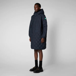 A person wearing the SAVE THE DUCK - VALERIAN PUFFER COAT in olive-green from the Recycled collection, along with a hood, black gloves, sunglasses, a bucket hat, black pants, and clogs. They are standing sideways and looking at the camera against a plain gray background.